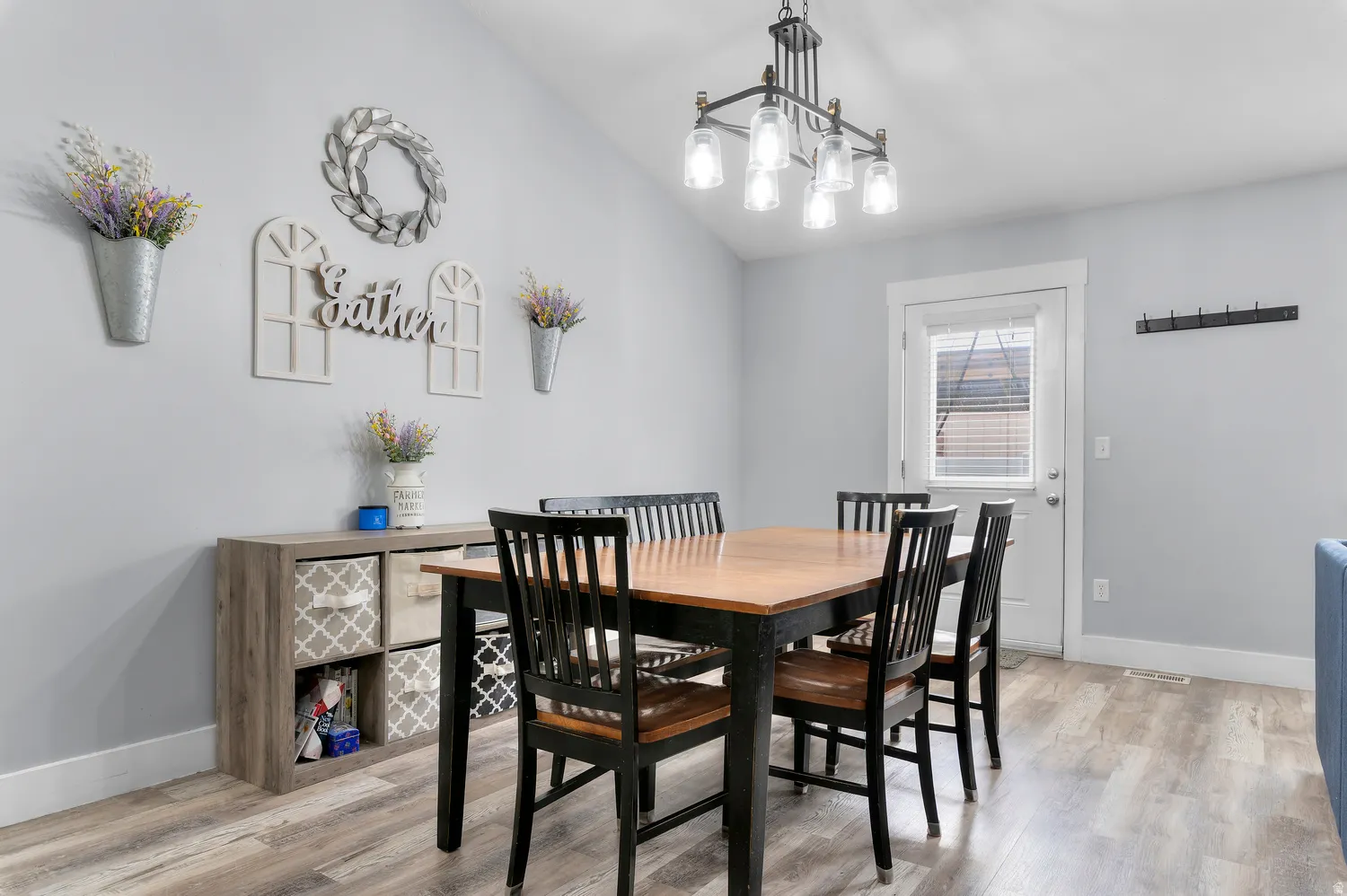 Vaulted ceiling with an industrial-style chandelier, light wood-finish flooring, and a glass-paneled exterior door
