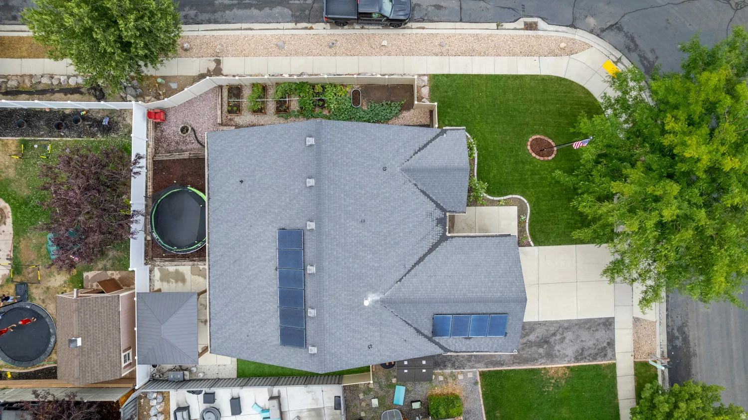 Gable roofline with solar panel arrays, expansive front yard with manicured lawn, concrete driveway, and established perimeter landscaping