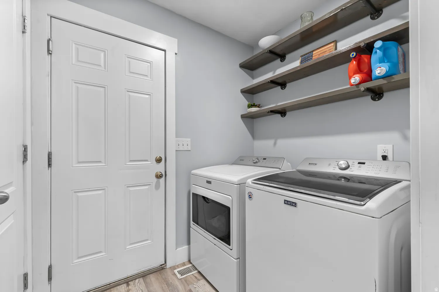 Laundry area featuring wood-finish flooring, light gray wall paint, and open shelving with industrial-style brackets