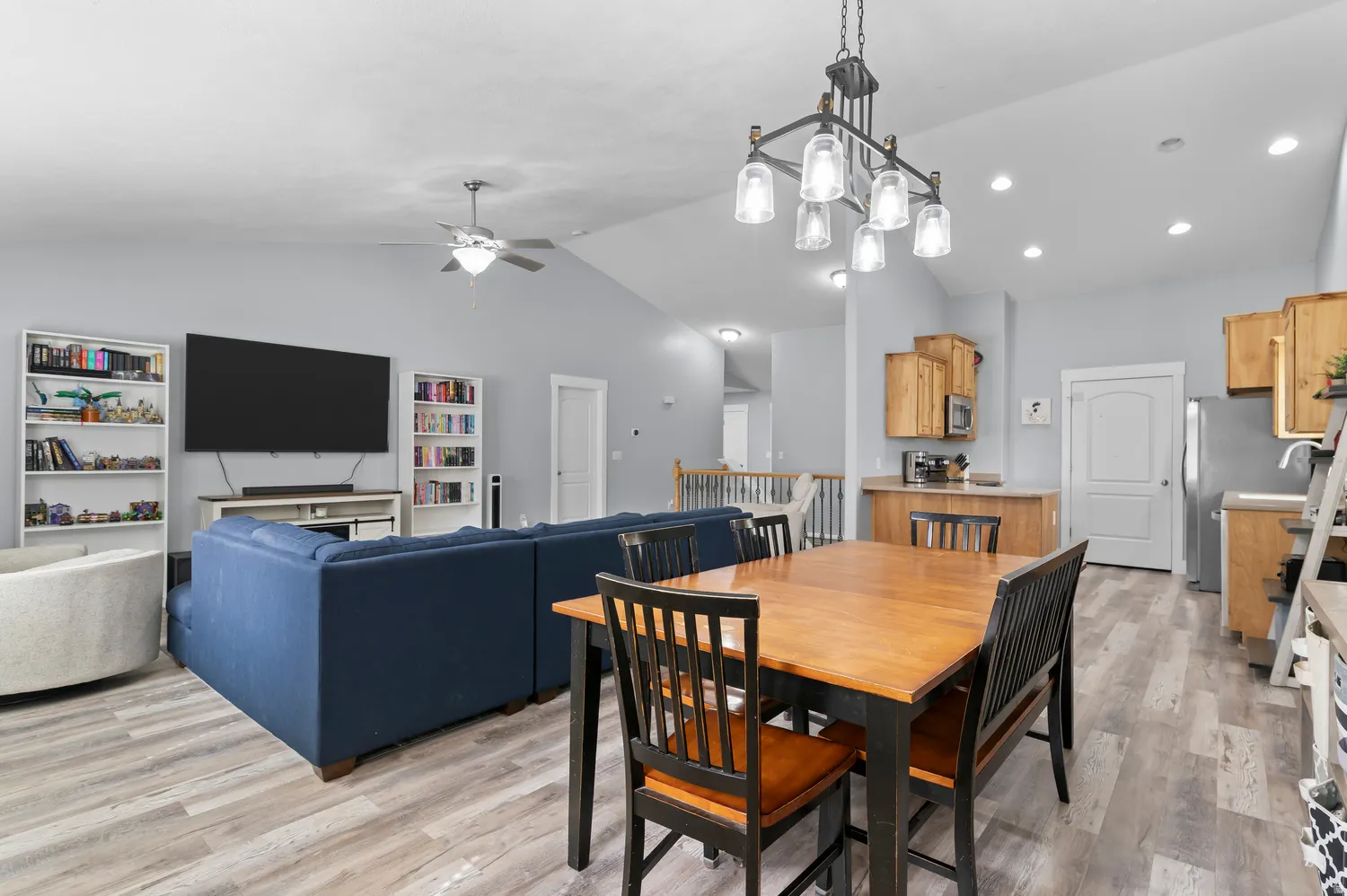 Vaulted ceilings with recessed lighting, wood-finish flooring, kitchen with wood cabinetry and stainless steel appliances, dining area with modern chandelier, and living area with ceiling fan