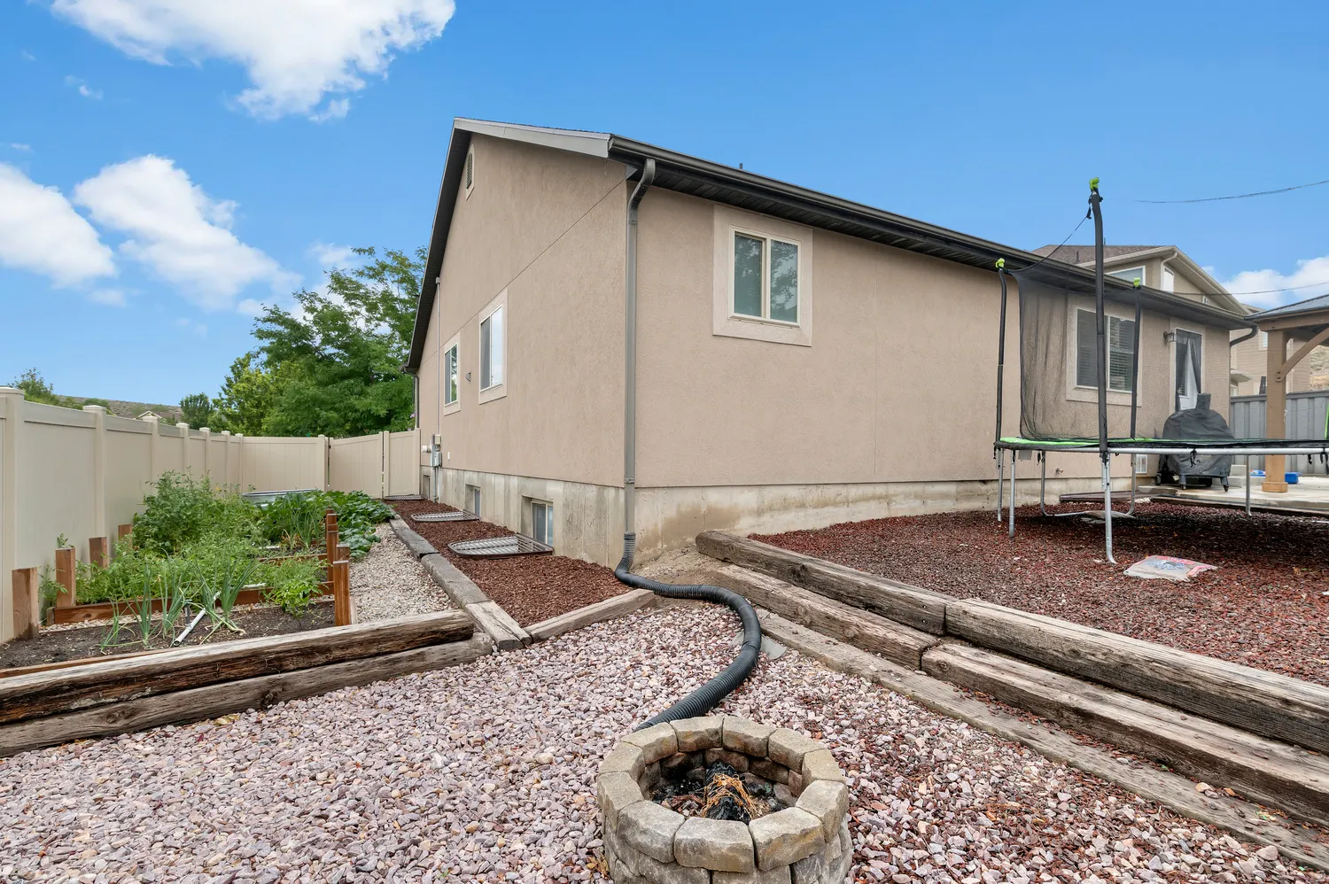 Stucco exterior with multiple windows, privacy fencing, a stone-finish fire pit, and a dedicated garden area with raised beds