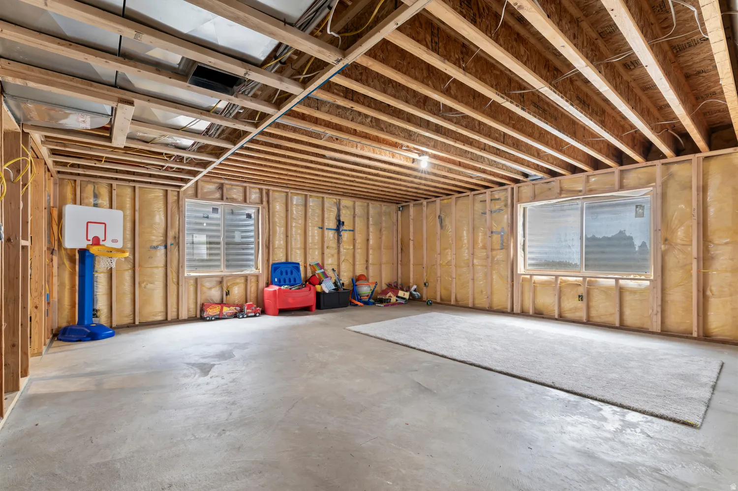 Unfinished basement with exposed wood framing, concrete flooring, and two window openings