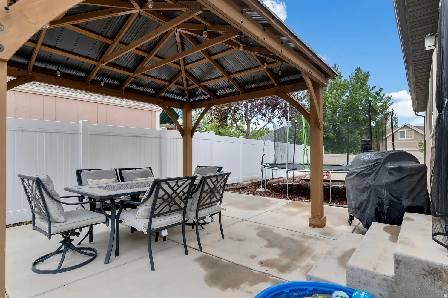 Concrete patio featuring a wood gazebo with a corrugated metal roof and exposed string lighting