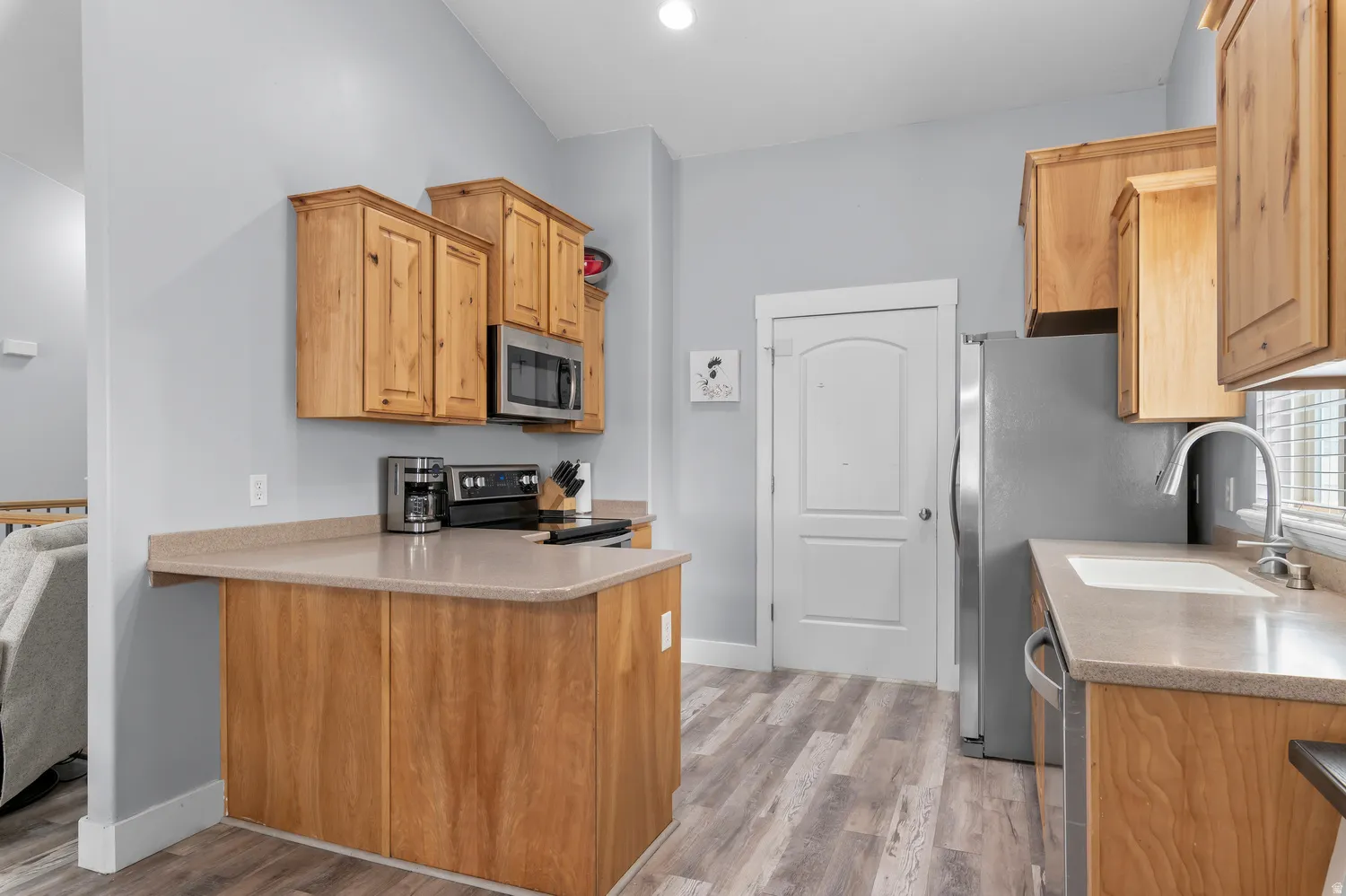 Kitchen featuring wood cabinetry, stainless steel appliances, a bar-height counter, a single-basin sink, and wood-finish flooring