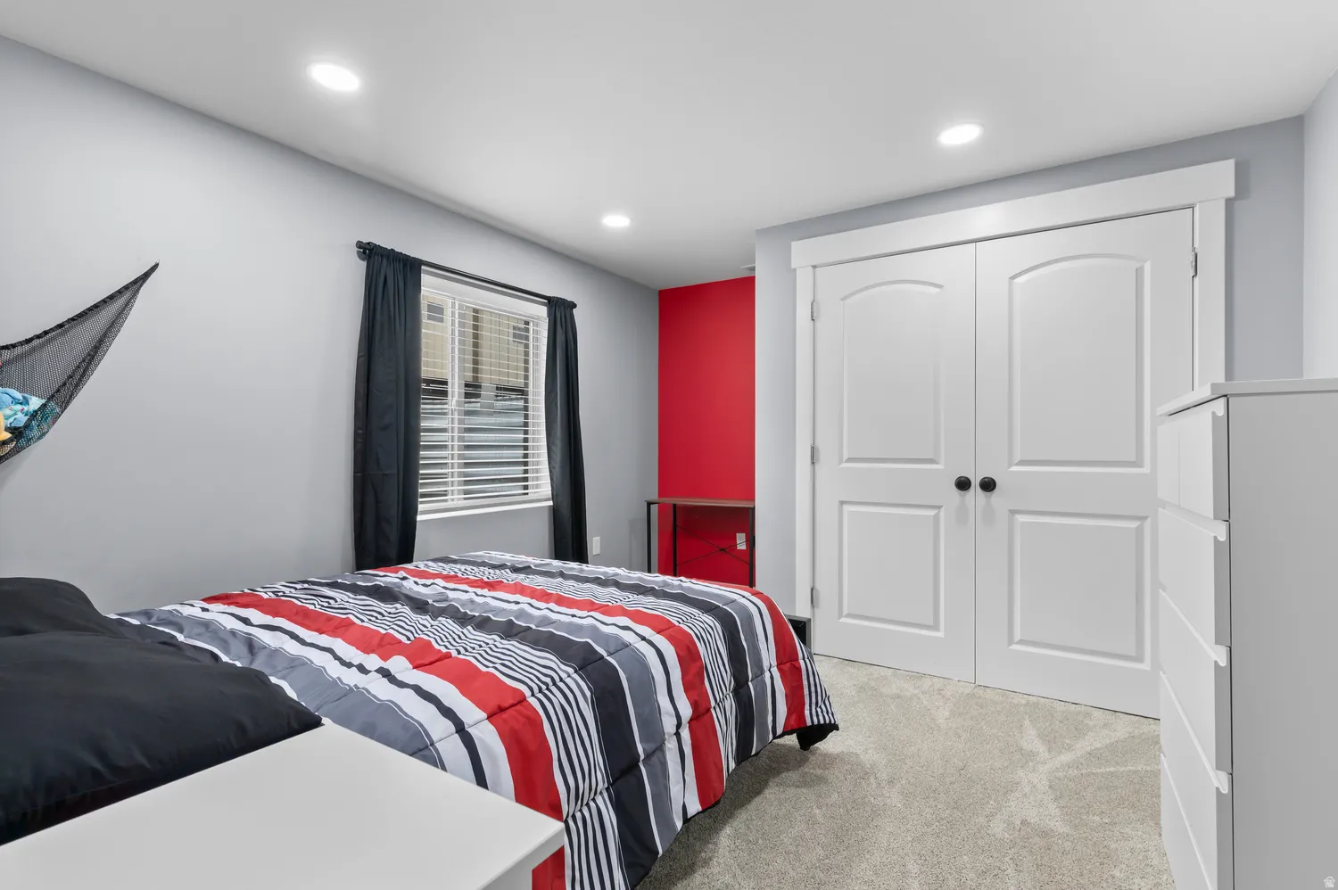 Recessed lighting illuminates a room with light gray walls, a red accent wall, and light gray carpet flooring