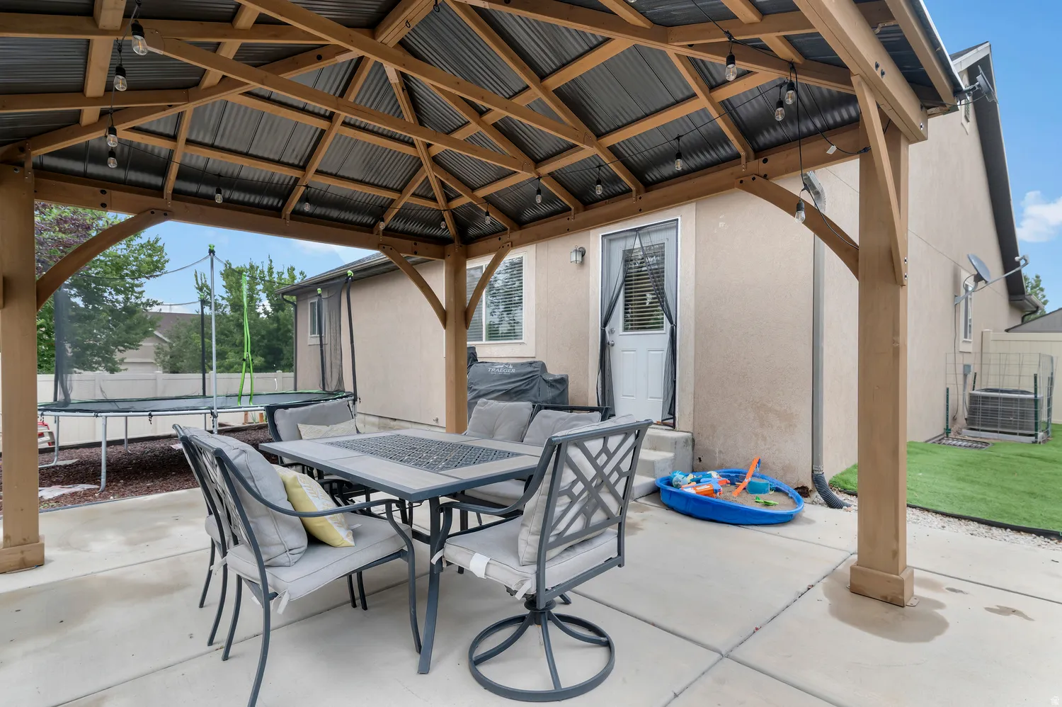 Expansive patio featuring a wood gazebo with a metal roof and string lights, complemented by a stucco exterior
