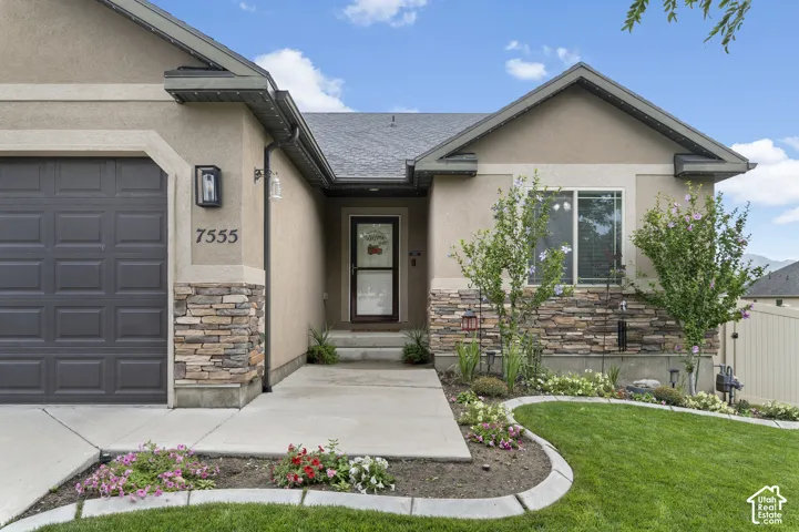 Stucco exterior with stone veneer accents, an attached garage, landscaped front yard, and covered entry