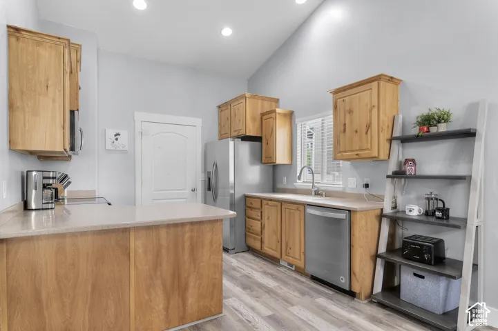 Kitchen featuring wood cabinetry, stainless steel appliances, light-toned countertops, and wood-finish flooring
