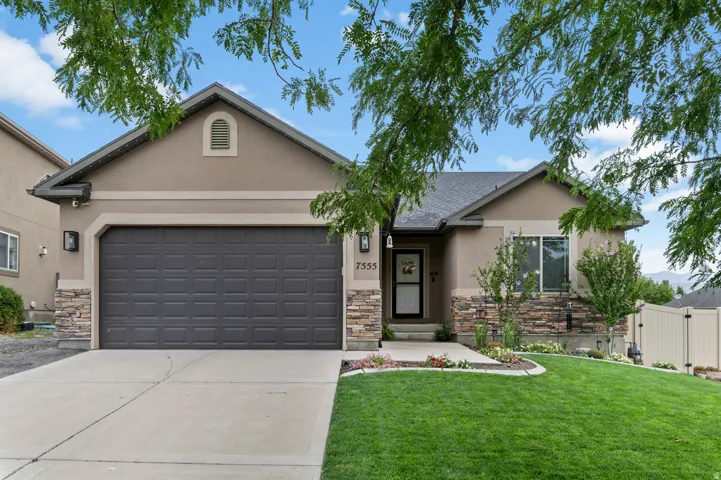 Stucco exterior with stone veneer accents, an attached garage, and a landscaped front yard with a curved lawn