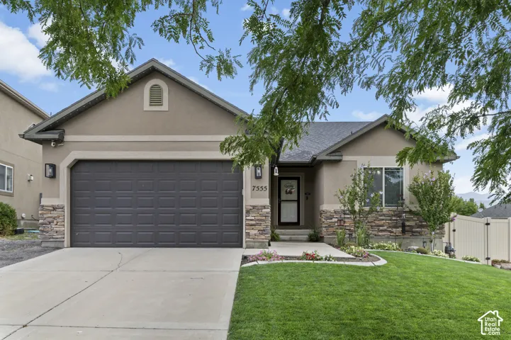 Stucco exterior with stone veneer accents, an attached garage, and a landscaped front yard with a curved lawn