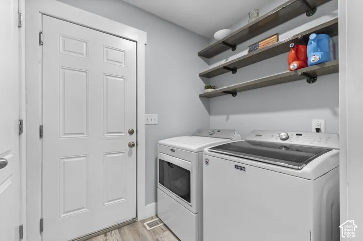 Laundry area featuring wood-finish flooring, light gray wall paint, and open shelving with industrial-style brackets