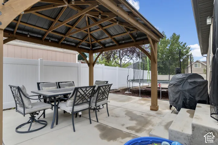 Concrete patio featuring a wood gazebo with a corrugated metal roof and exposed string lighting
