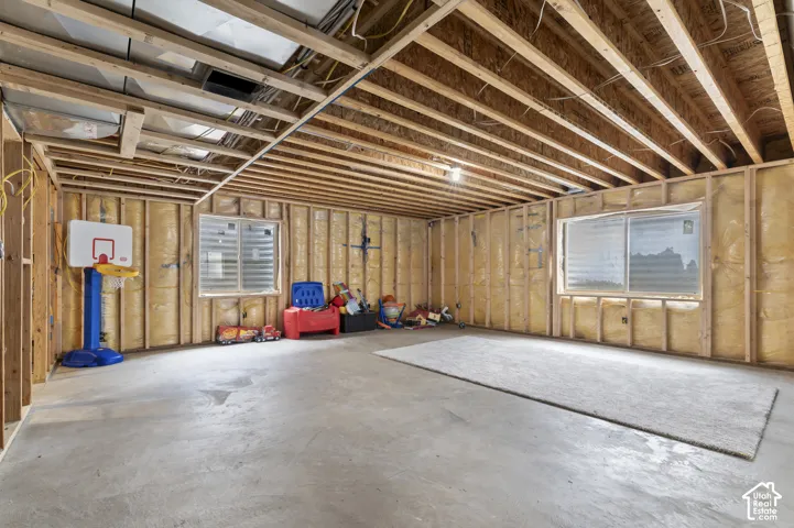 Unfinished basement with exposed wood framing, concrete flooring, and two window openings