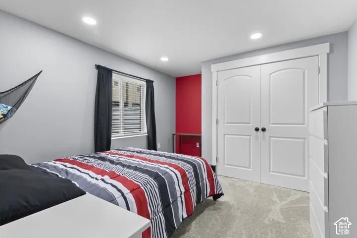 Recessed lighting illuminates a room with light gray walls, a red accent wall, and light gray carpet flooring
