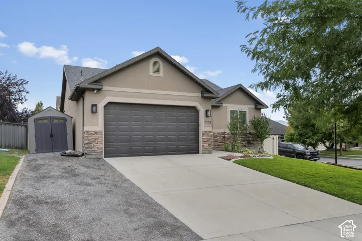 Stucco exterior with stone accents, a two-car garage, a concrete driveway, a separate gravel parking area, and a storage shed