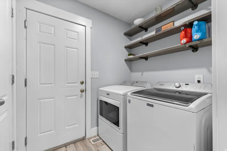 Laundry area featuring wood-finish flooring, light gray wall paint, and open shelving with industrial-style brackets