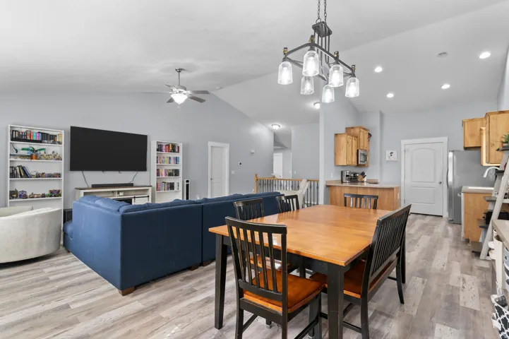 Vaulted ceilings with recessed lighting, wood-finish flooring, kitchen with wood cabinetry and stainless steel appliances, dining area with modern chandelier, and living area with ceiling fan