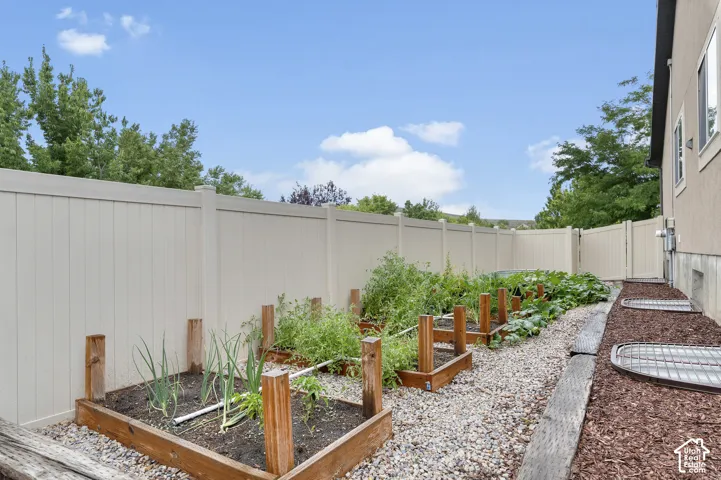 Raised garden beds with established plantings, full-height privacy fencing, gravel pathway, and mulched landscaping