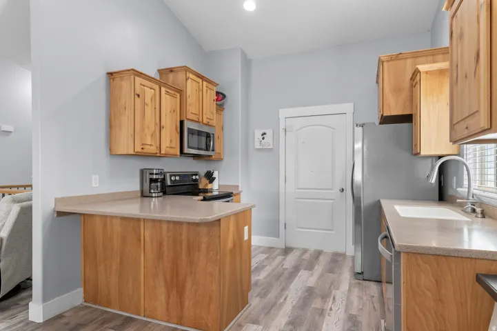Kitchen featuring wood cabinetry, stainless steel appliances, a bar-height counter, a single-basin sink, and wood-finish flooring