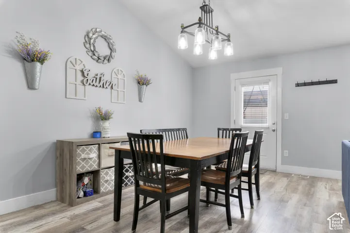 Vaulted ceiling with an industrial-style chandelier, light wood-finish flooring, and a glass-paneled exterior door