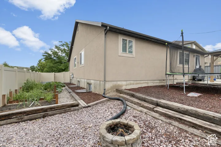 Stucco exterior with multiple windows, privacy fencing, a stone-finish fire pit, and a dedicated garden area with raised beds