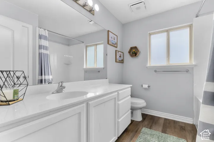 Full-width vanity mirror, white shaker-style cabinetry, white solid surface countertop, wood-finish flooring, and a window with privacy glass