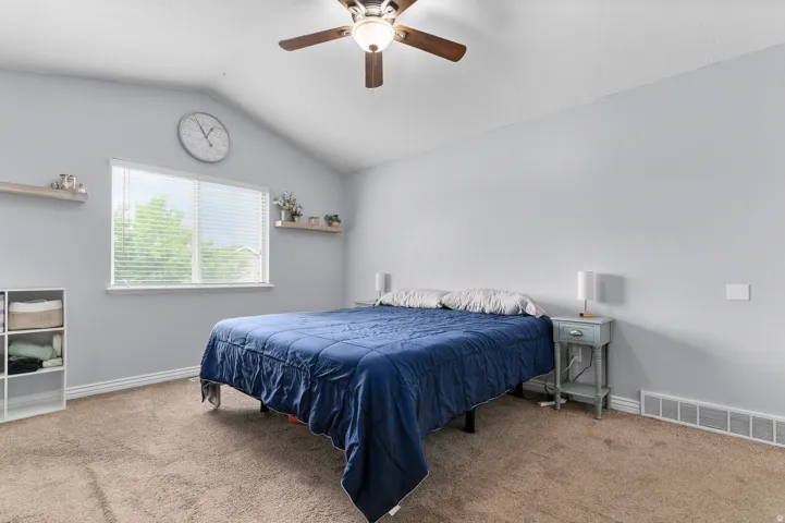 Angled ceiling with a ceiling fan, window with blinds, and wall-mounted shelving