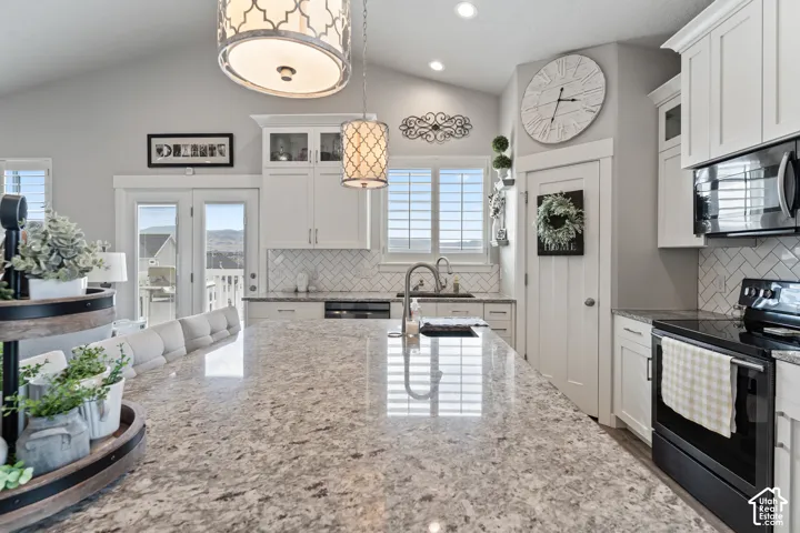 Vaulted ceilings, a spacious kitchen island with a stone countertop, white shaker cabinetry, stainless steel appliances, and French doors