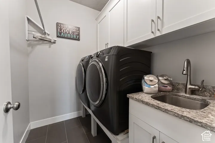 White shaker-style cabinetry with brushed nickel hardware, stone countertop, undermount stainless steel sink with gooseneck faucet, and dark tile flooring