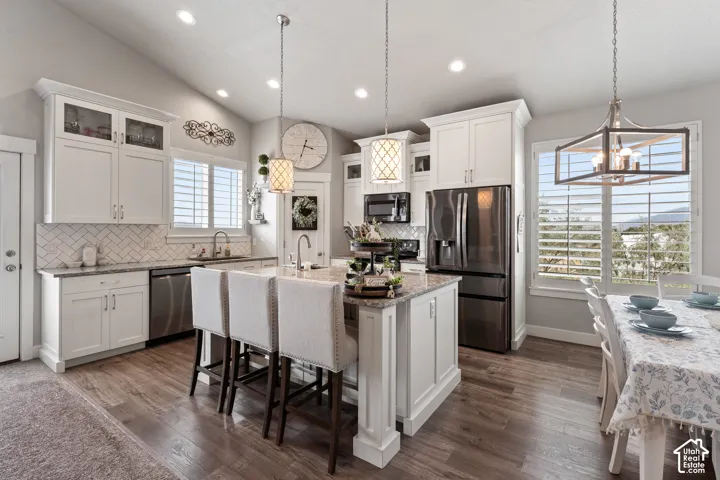 Vaulted ceilings, white shaker cabinetry, stainless steel appliances, wood-finish flooring, and a kitchen island with seating