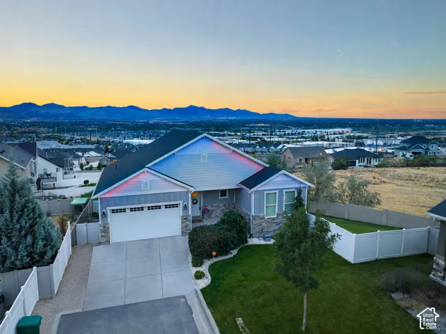 Siding exterior with stone accents, attached two-car garage, concrete driveway, fenced yard, and mountain backdrop
