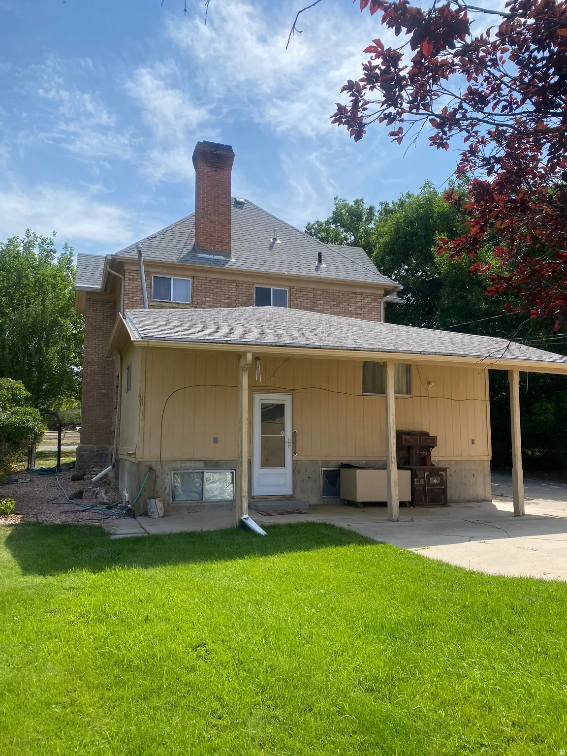 Brick exterior with a large chimney, covered patio, and a manicured lawn