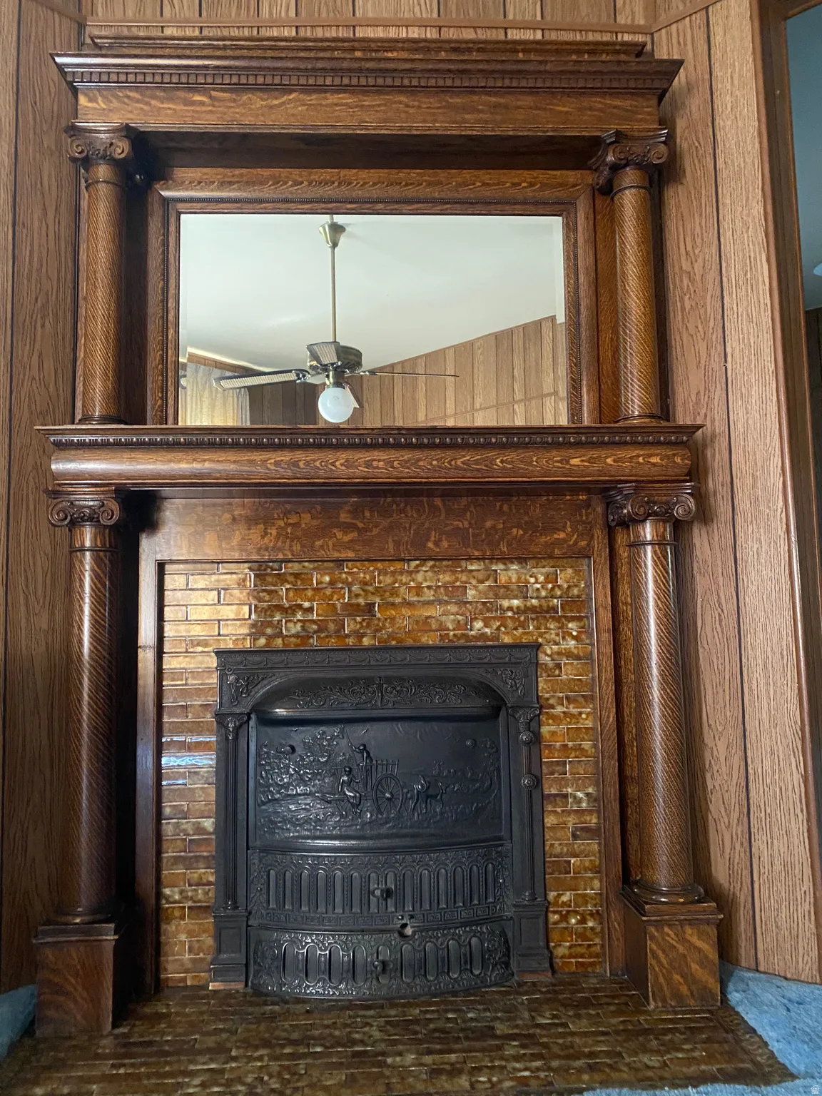 Ornate wood-finish fireplace surround with fluted columns and carved details, featuring a decorative cast iron firebox and a brick-finish hearth