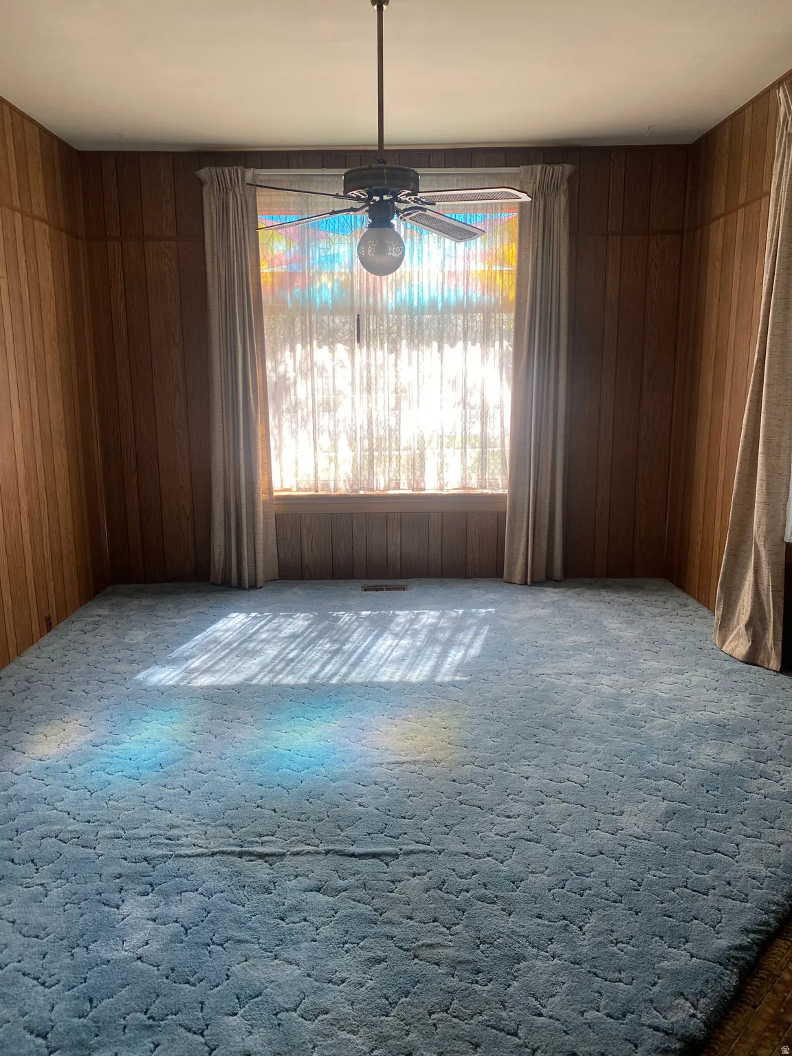 Wood-paneled walls with a central window, featuring a ceiling fan with light fixture