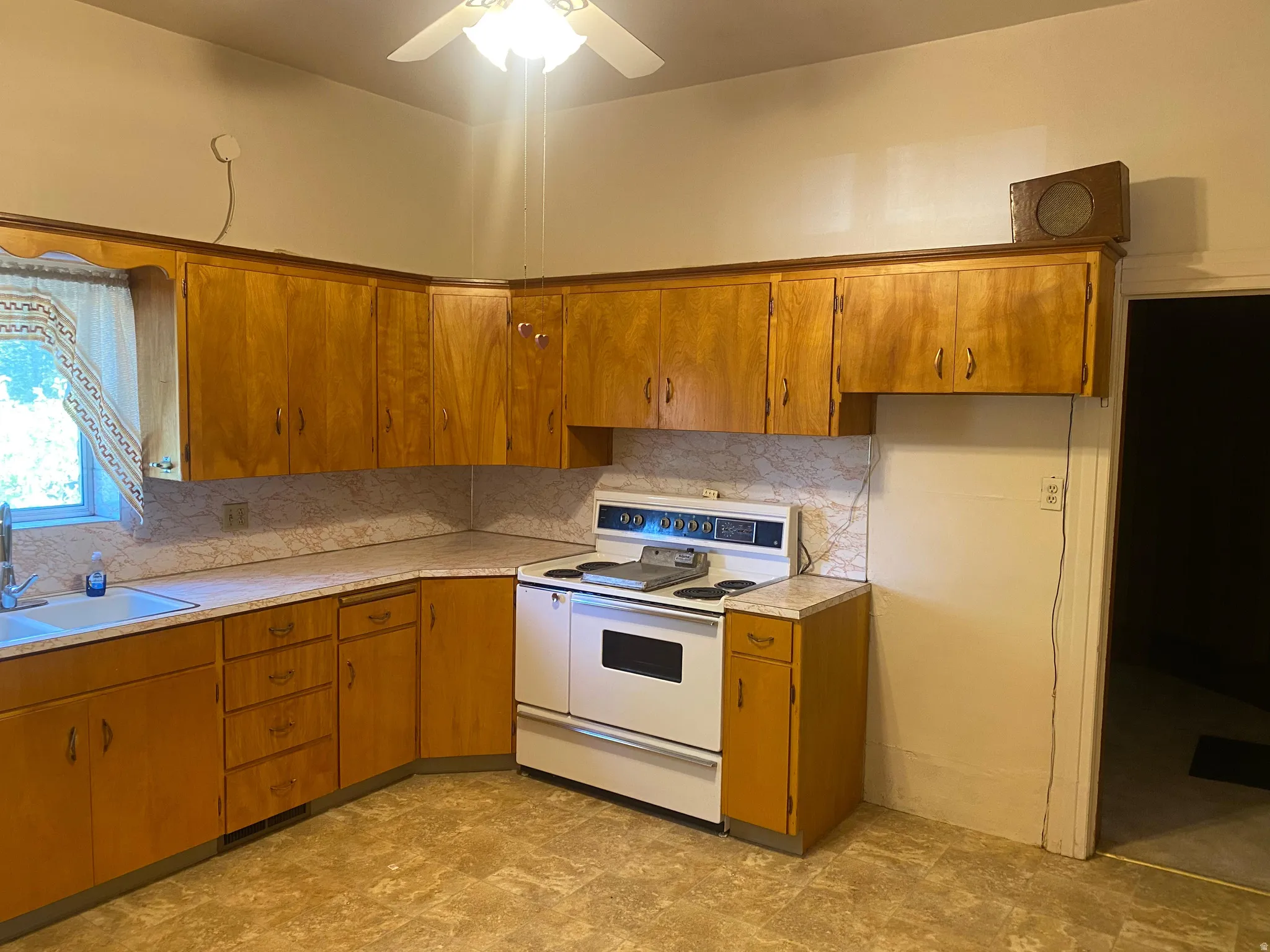 U-shaped kitchen featuring wood-finish cabinetry, a corner sink with a window, and a white electric range