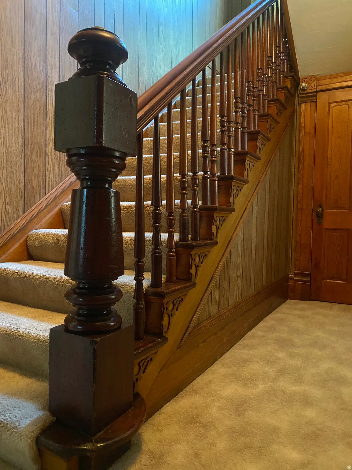 Carpeted staircase with an ornate wood newel post and balusters