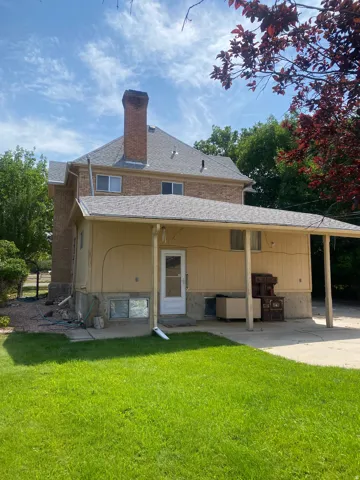 Brick exterior with a large chimney, covered patio, and a manicured lawn