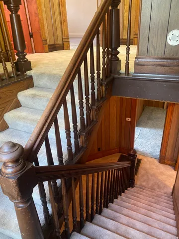 Wood-paneled staircase featuring an intricate baluster design and carpeted treads