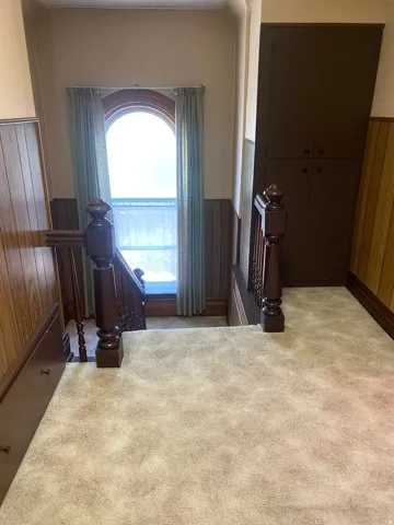 Arched window with drapes, wood paneling, built-in cabinetry, and carpeted floor