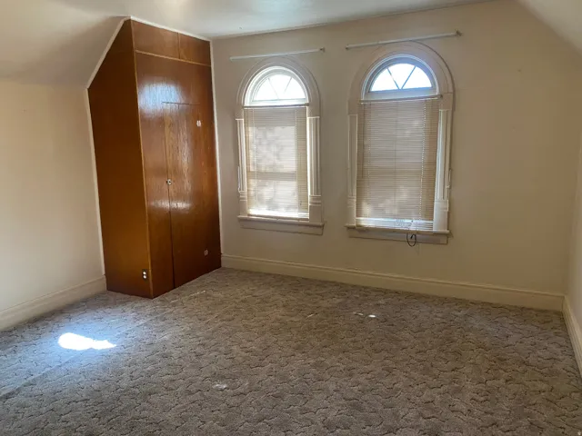 Arched windows, wood-finish built-in cabinetry, sloped ceiling, and carpeted flooring