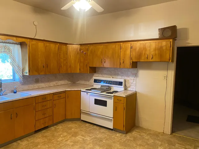 U-shaped kitchen featuring wood-finish cabinetry, a corner sink with a window, and a white electric range