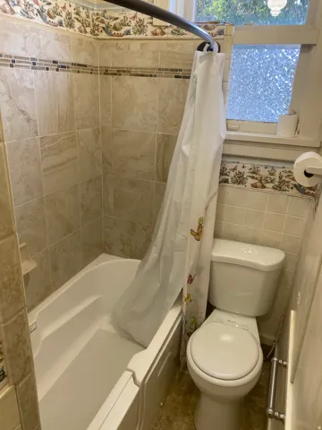 White bathtub with integrated steps, surrounded by beige wall tiles with a decorative mosaic band