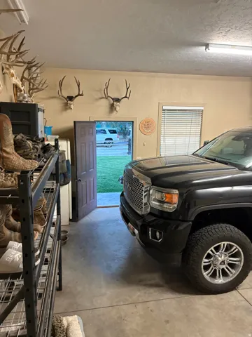 Garage space with concrete flooring, a solid door, and a single window with horizontal blinds