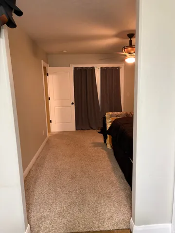 Neutral tone wall paint, light-colored carpeting, white paneled doors, and a ceiling fan with integrated lighting