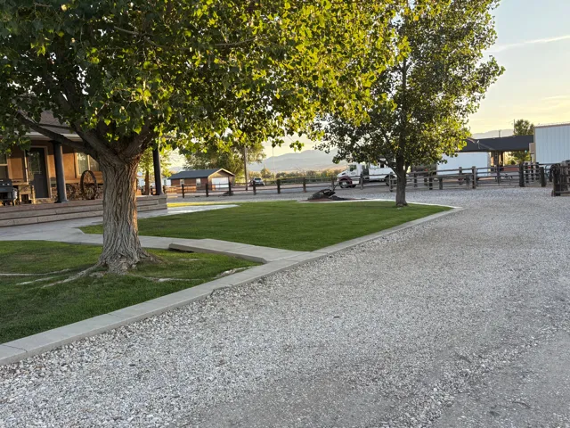 Expansive gravel driveway bordered by a concrete curb, mature trees, and a manicured lawn