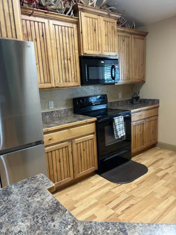Stainless steel refrigerator, black range, built-in black microwave, wood-finish cabinetry, and laminate countertops