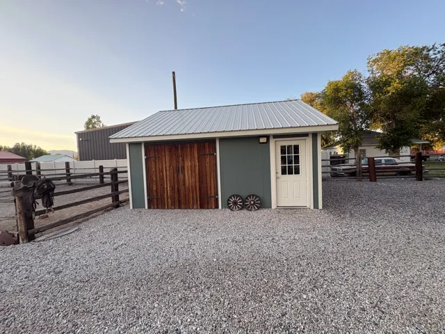 Gravel lot featuring a detached outbuilding with a metal roof, paneled siding, wood barn doors, and a paneled entry door