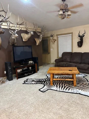 Vaulted ceiling, ceiling fan with integrated lighting, wall-to-wall carpeting, window with blinds, and a solid door