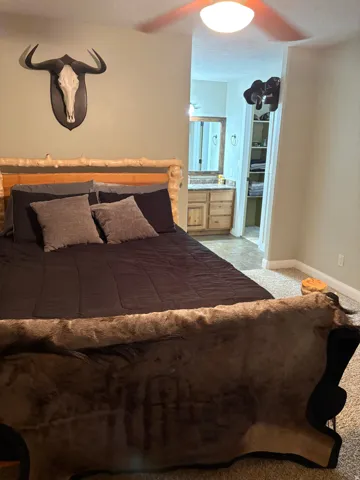 Bedroom with ceiling fan, carpet flooring, and an attached bathroom featuring a wood-finish vanity with a countertop and built-in mirror
