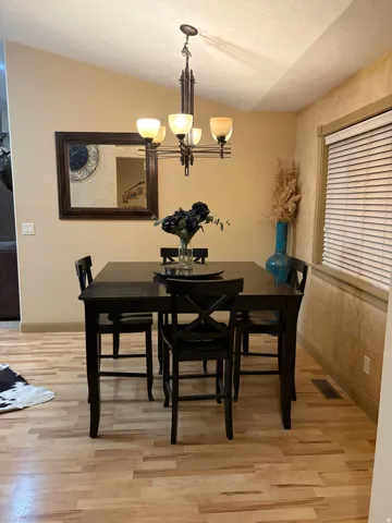 Wood-finish flooring, vaulted ceiling, multi-light chandelier, and window with blinds